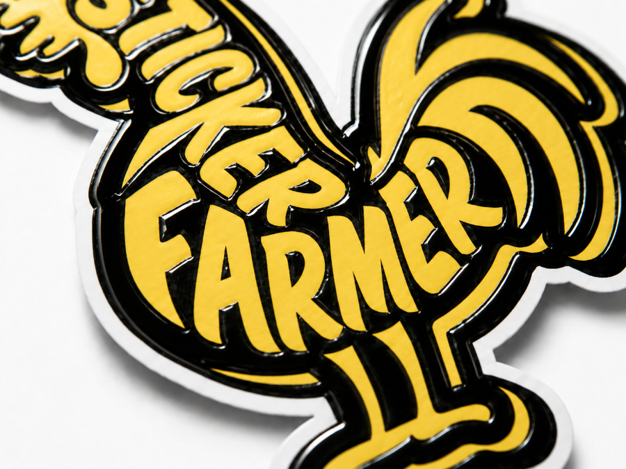 Close-up of a die-cut sticker with bold yellow “Sticker Farmer” lettering and a rooster shape, finished with shiny 2-pass spot UV coating.