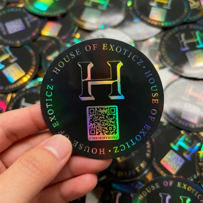 Holographic sticker with 'House of Exoticz' branding held by a hand, surrounded by more stickers.
