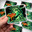 Sticker of the Statue of Liberty eating a pizza held by a hand, with more stickers in the background.