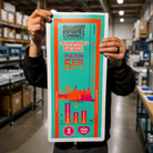 Large custom vinyl label with a colorful teal and orange product packaging design held inside a print shop.